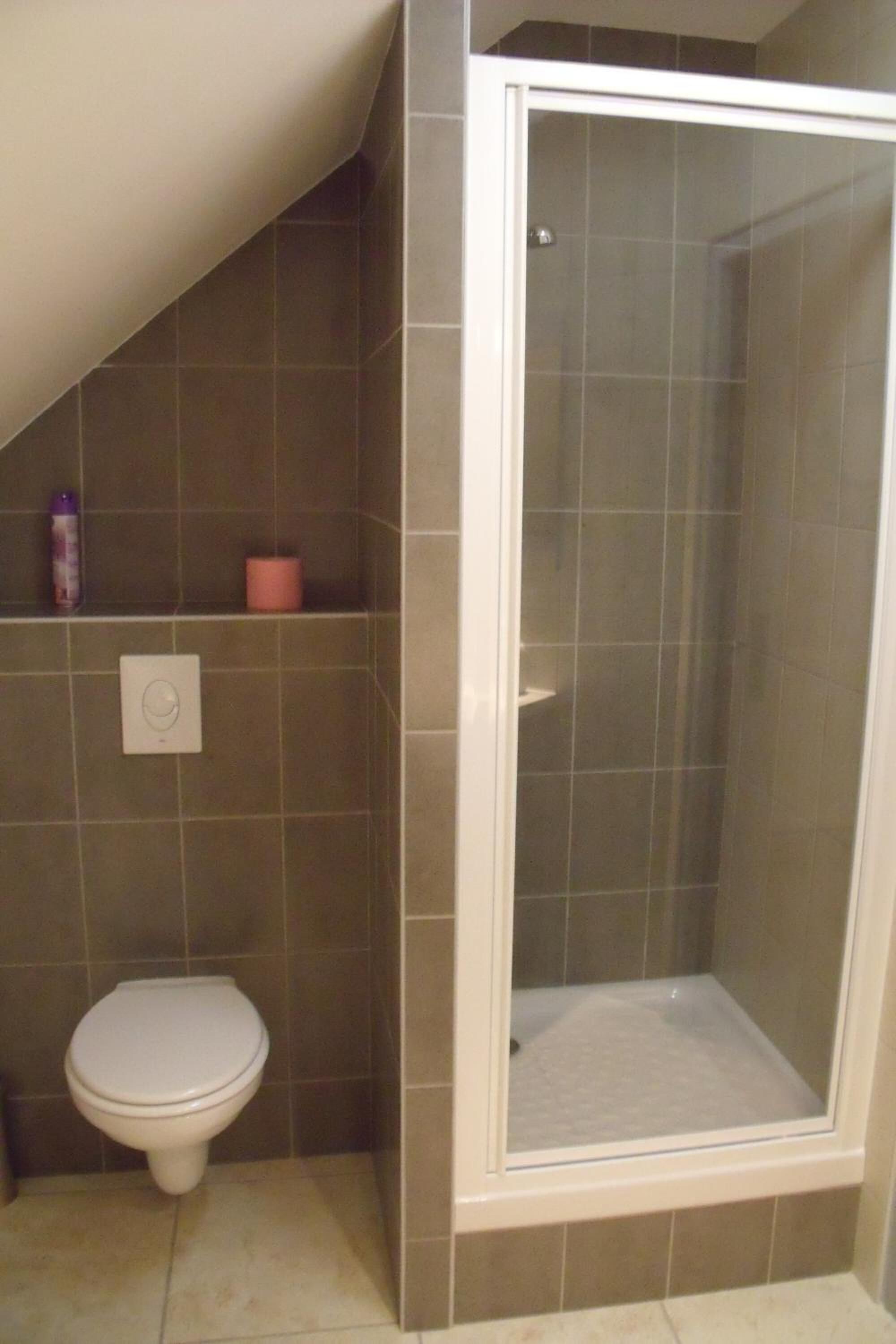 Une salle de bain équipée d’une douche, de toilettes et d’une étagère où sont rangés les articles de toilette.