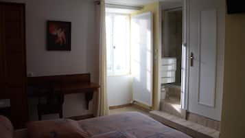 A bedroom with a bed, a desk, and a bathroom visible through an open door.
