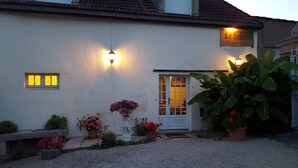 A white building with a tiled roof, a door with glass panels, and a sign above the door. There are potted plants and flowers in front of the building. - Maison D'Hote Le Relais (Fresnes)