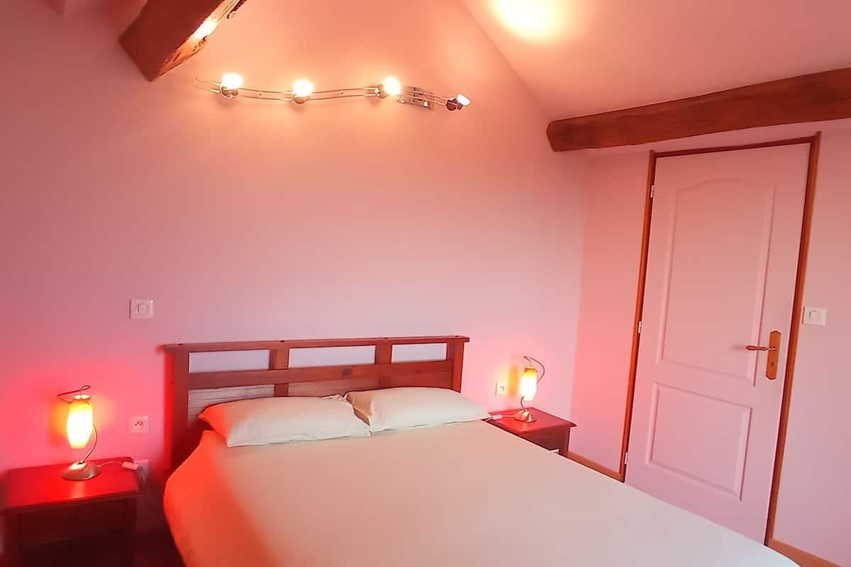 A bedroom with a wooden bed, bedside lamps, a door, and a wall-mounted light fixture.