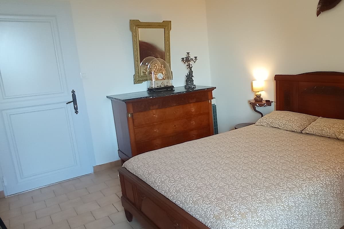 A bedroom with a wooden bed, a dresser, a mirror, and two wall-mounted lamps.