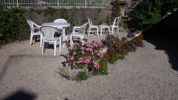An outdoor seating area with white plastic chairs and tables, surrounded by gravel and potted plants with pink and orange flowers.