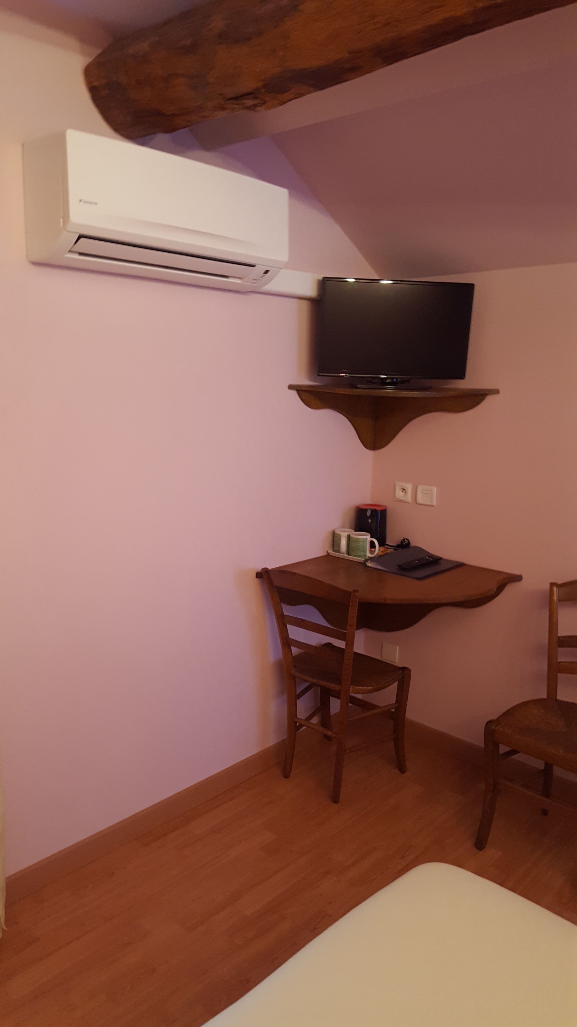 A small room with a wooden desk, a television mounted on a wooden shelf, a chair, and a bed.