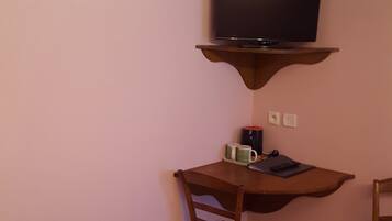 A small room with a wooden desk, a television mounted on a wooden shelf, a chair, and a bed.