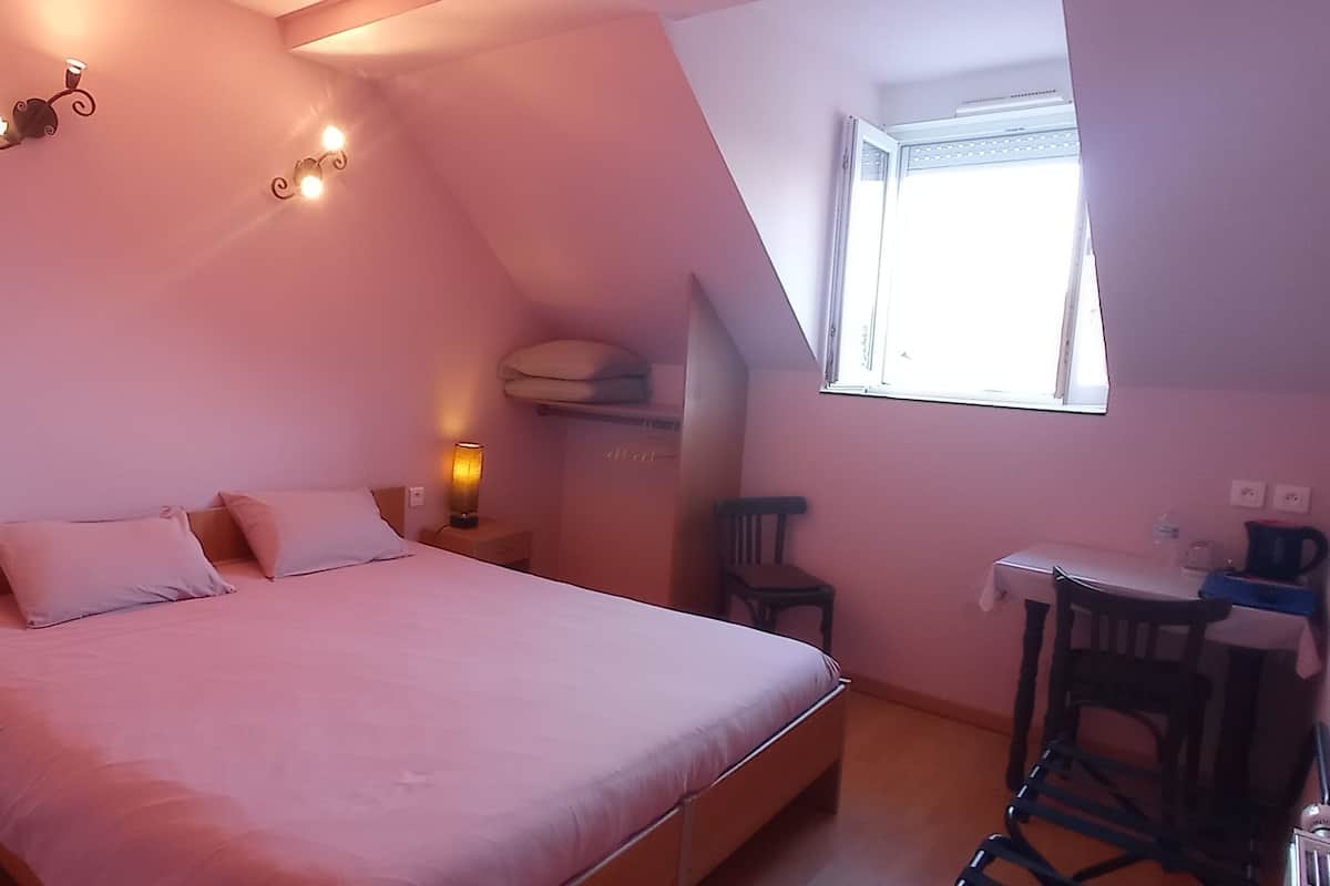 A bedroom with a bed, bedside lamps, a chair, a small table, and a window.