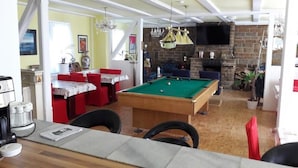 Un salon chaleureux avec une table de billard, un coin repas avec des chaises rouges et une cheminée.