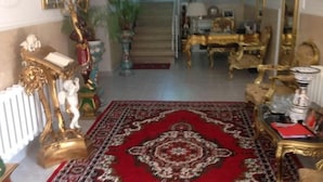 Un vaste hall d’entrée agrémenté de meubles richement décorés, d’un tapis rouge à motifs et d’un escalier menant à l’étage supérieur.