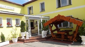 Un bâtiment jaune avec une enseigne indiquant « hôtel-restaurant ». On aperçoit une structure en bois à l’avant, qui pourrait être un élément décoratif ou faire partie de l’entrée.