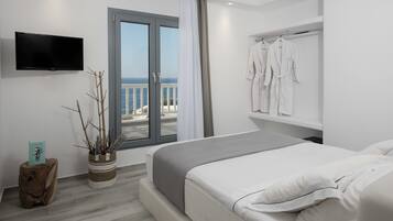 Ett modernt hotellrum med en stor säng, en platt-TV som är monterad på väggen, ett fönster med utsikt över havet och ett ställ med vita badrockar.