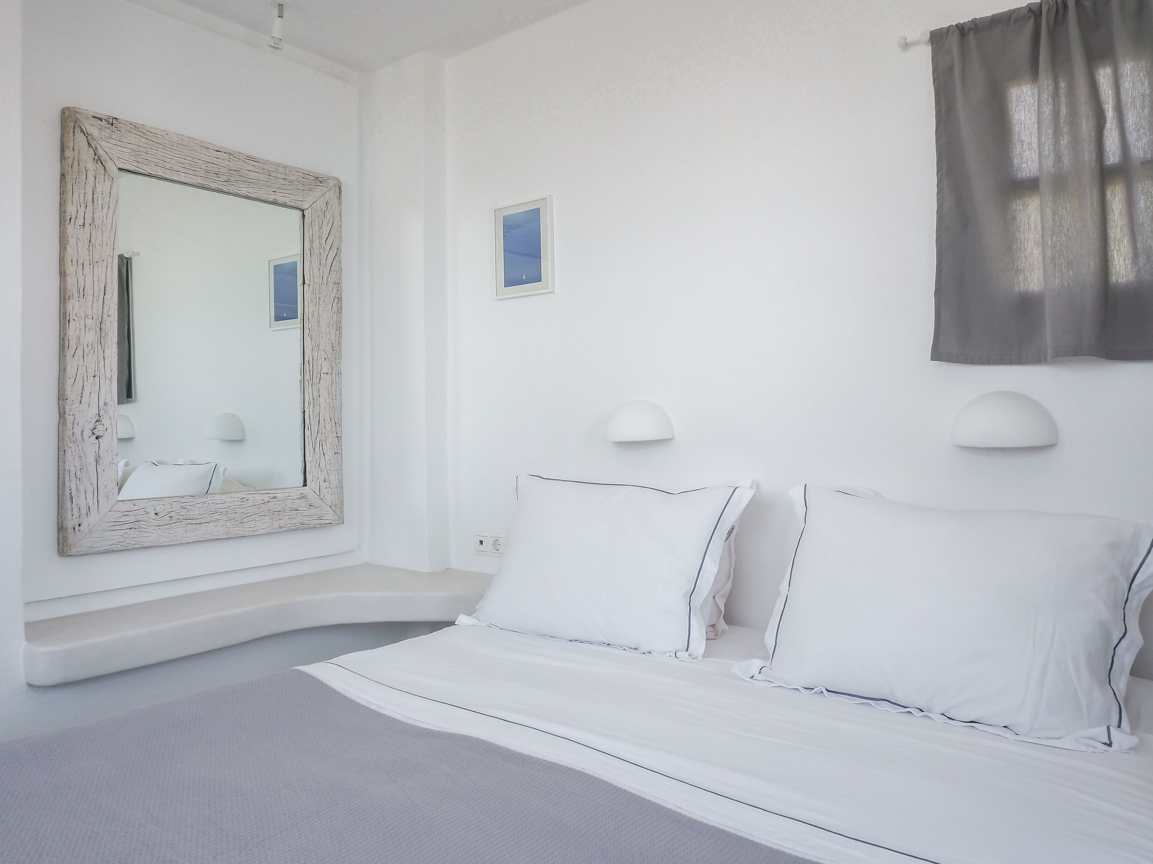 Une chambre à coucher blanche avec un grand miroir, deux lampes de chevet et un lit recouvert de linge de lit blanc.