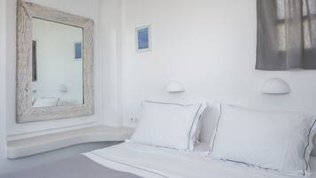 Une chambre à coucher blanche avec un grand miroir, deux lampes de chevet et un lit recouvert de linge de lit blanc.