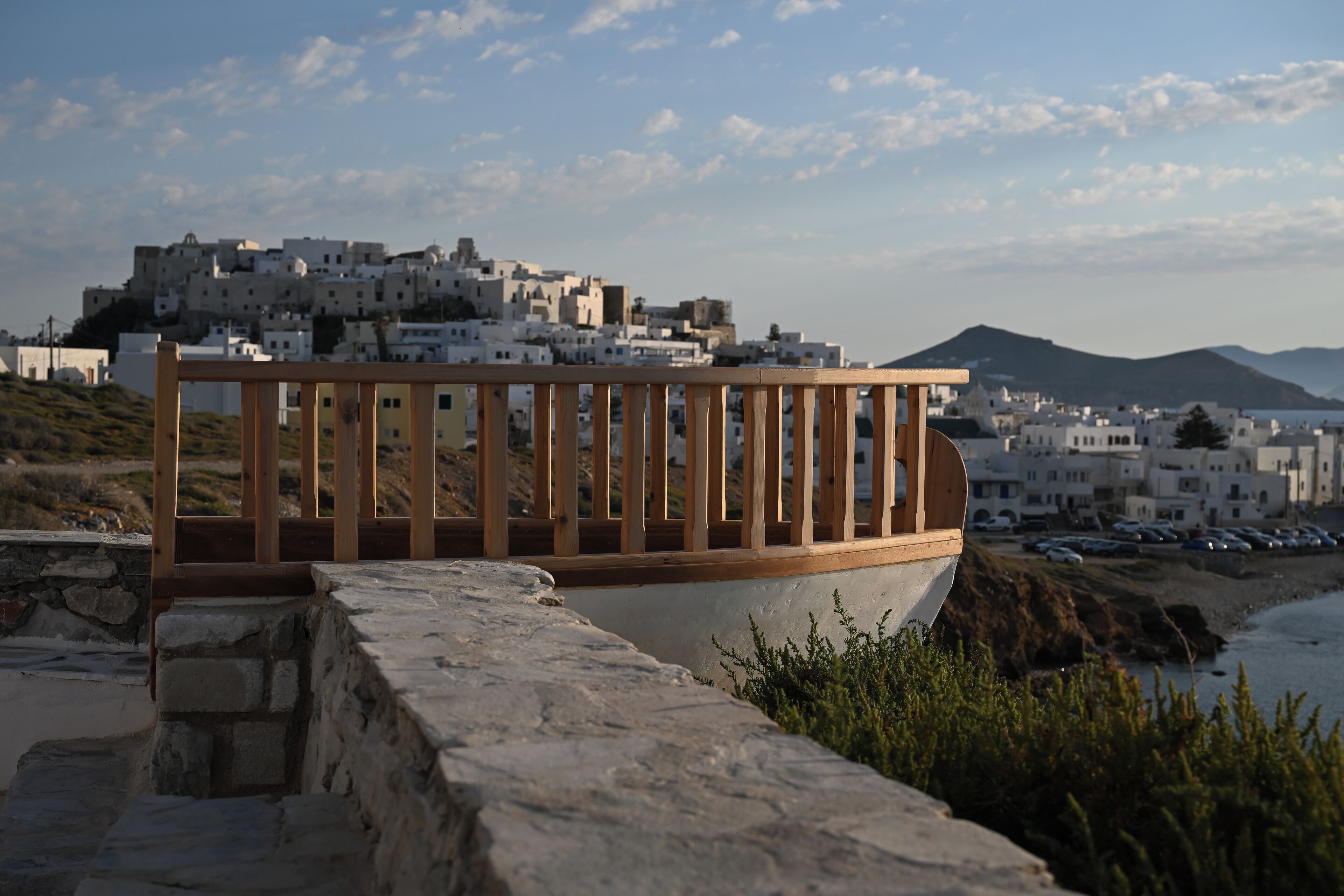A wooden deck overlooking a coastal town with white buildings and a mountain in the background.