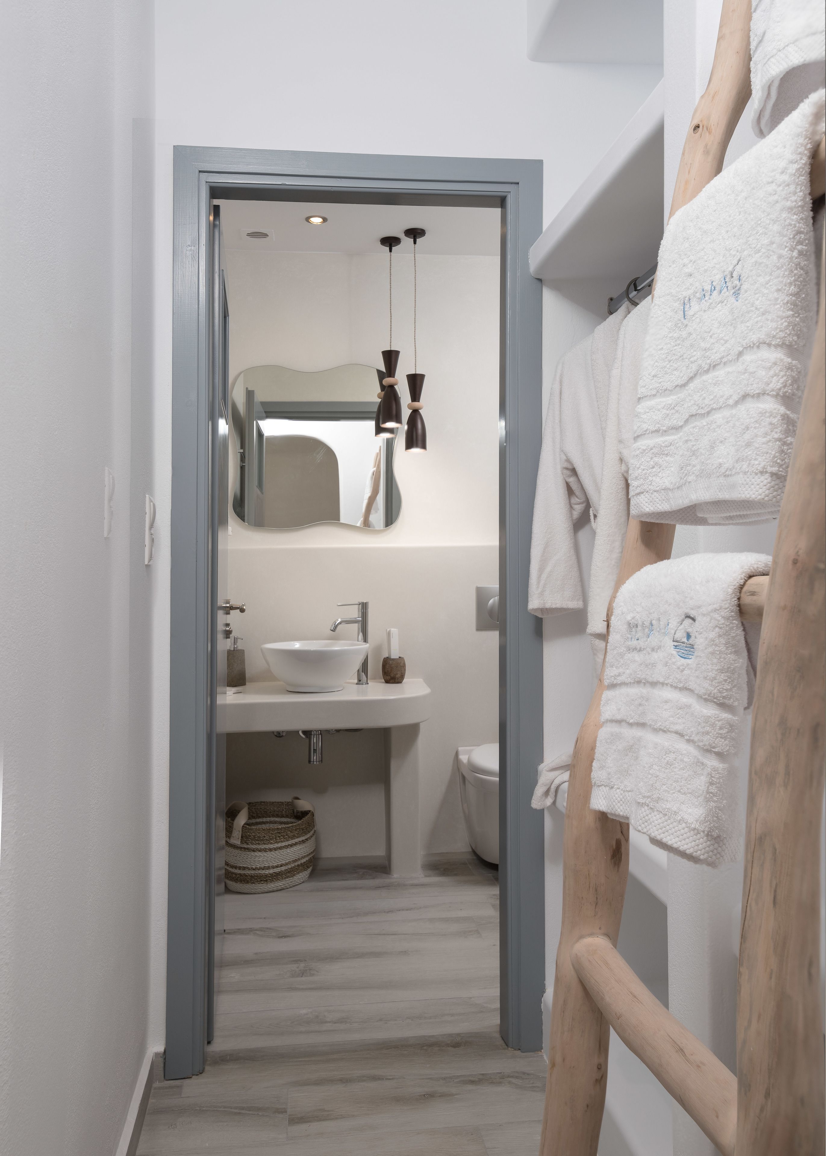 A modern bathroom with a white sink, mirror, and toilet. There is a wooden towel rack with towels hanging on it.