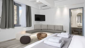 A modern hotel room with a large bed, a seating area, a flat-screen TV, and a bathroom with a mirror and sink.