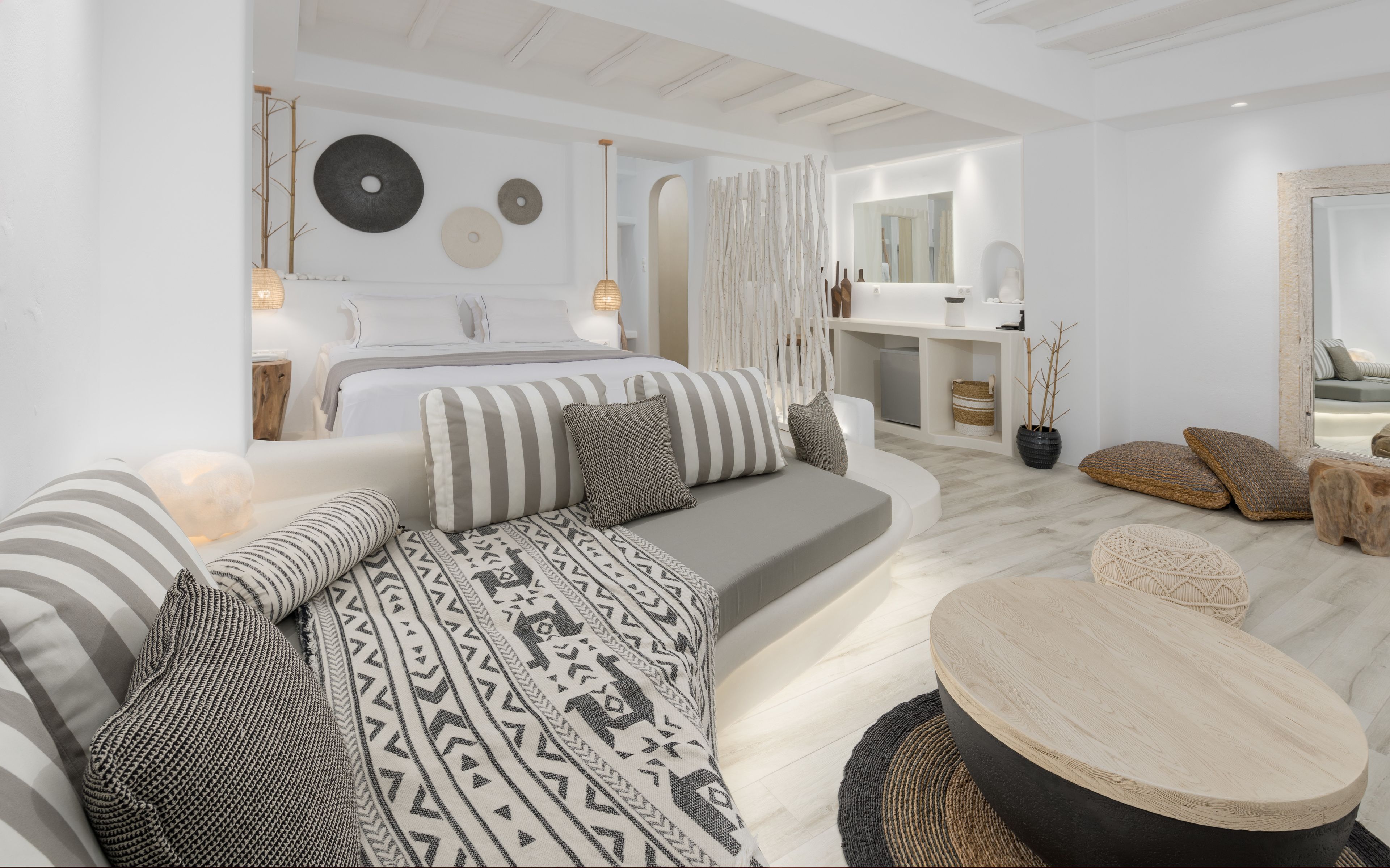 Una sala moderna con un sofá, una mesa redonda de centro y una cama con almohadones a rayas.
