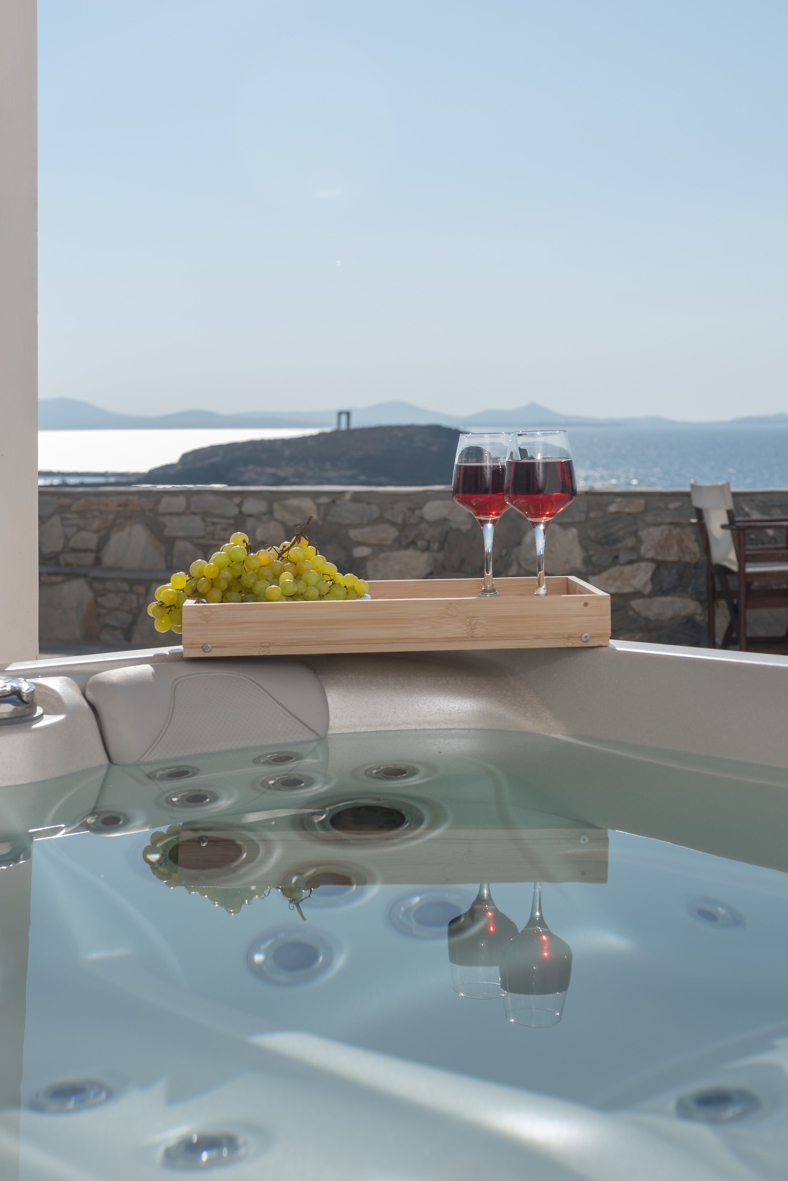 Ein Whirlpool mit einer Holztablett, auf dem gelbe Trauben und zwei Gläser Rotwein stehen, mit Blick auf eine Steinmauer und eine schöne Aussicht.