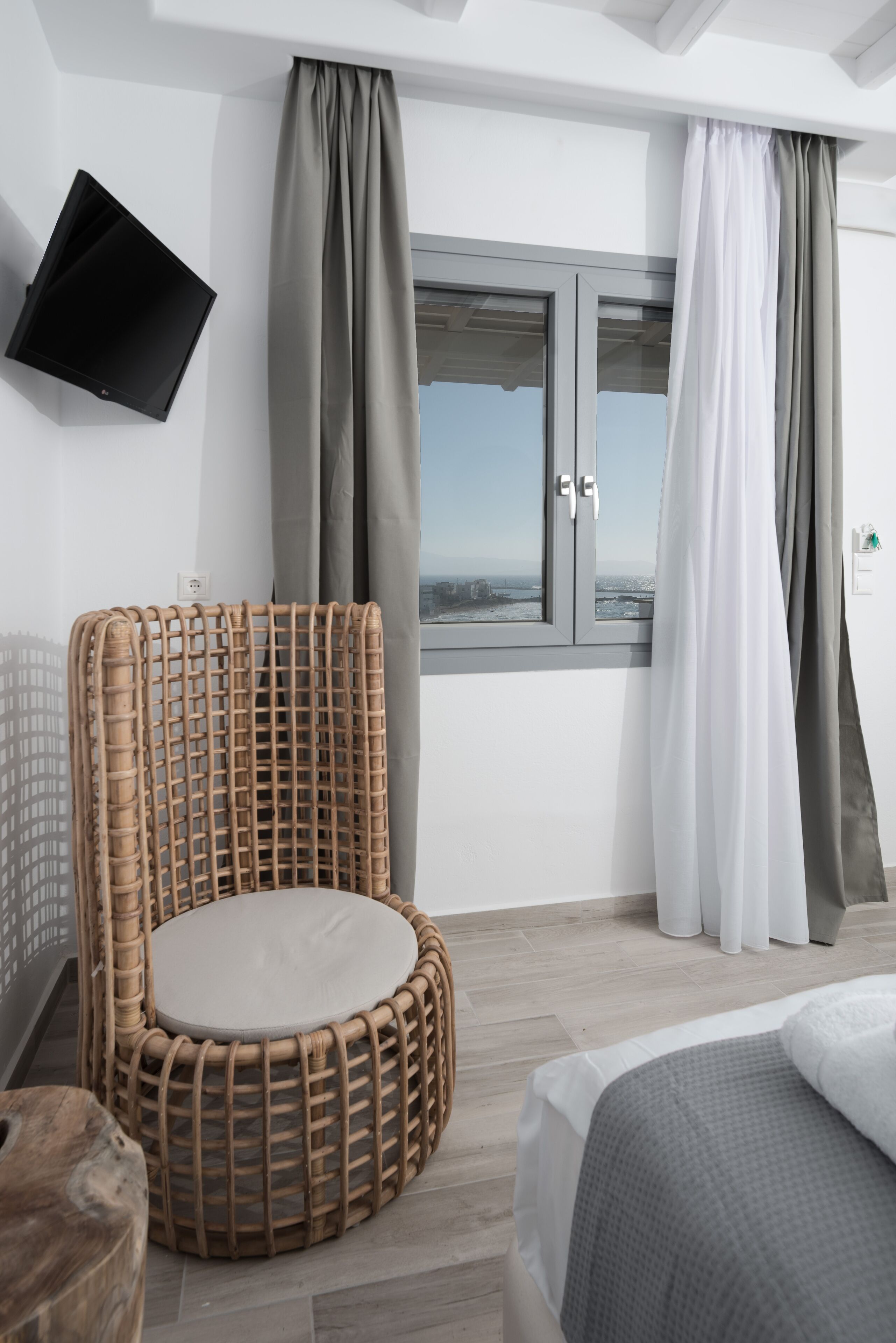Una habitación moderna con una silla de mimbre, una cama, un televisor de pantalla plana y una ventana con cortinas.