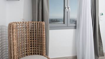 Una habitación moderna con una silla de mimbre, una cama, un televisor de pantalla plana y una ventana con cortinas.