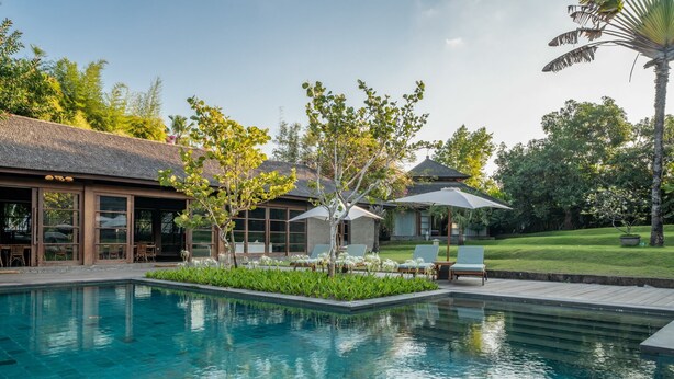 A swimming pool with lounge chairs and umbrellas, surrounded by greenery and a building with large windows. - 7BR Villa For Large Groups W/Pool Table, Canggu! 9Min Drive To Seminyak Square! (Canggu)