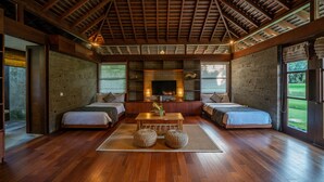 A spacious room with a high ceiling, wooden beams, a fireplace, two beds, a coffee table, and large windows offering a view of the outdoors. - 7BR Villa For Large Groups W/Pool Table, Canggu! 9Min Drive To Seminyak Square! (Canggu)