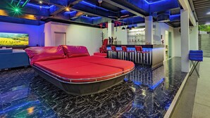 A modern hotel room with a red bed, a bar area, and a large TV displaying a scenic landscape. - Private Pool Villa for your family and friends / Private Chef available (Tambon Chalong)