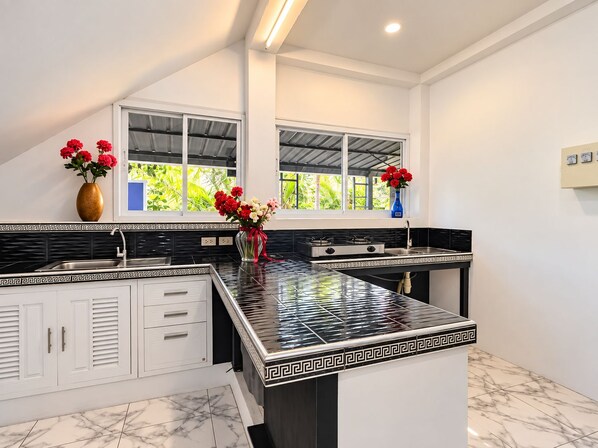 Una cucina moderna con zoccolo a mosaico bianco e nero, mobili bianchi e un'isola centrale con piano di lavoro nero.