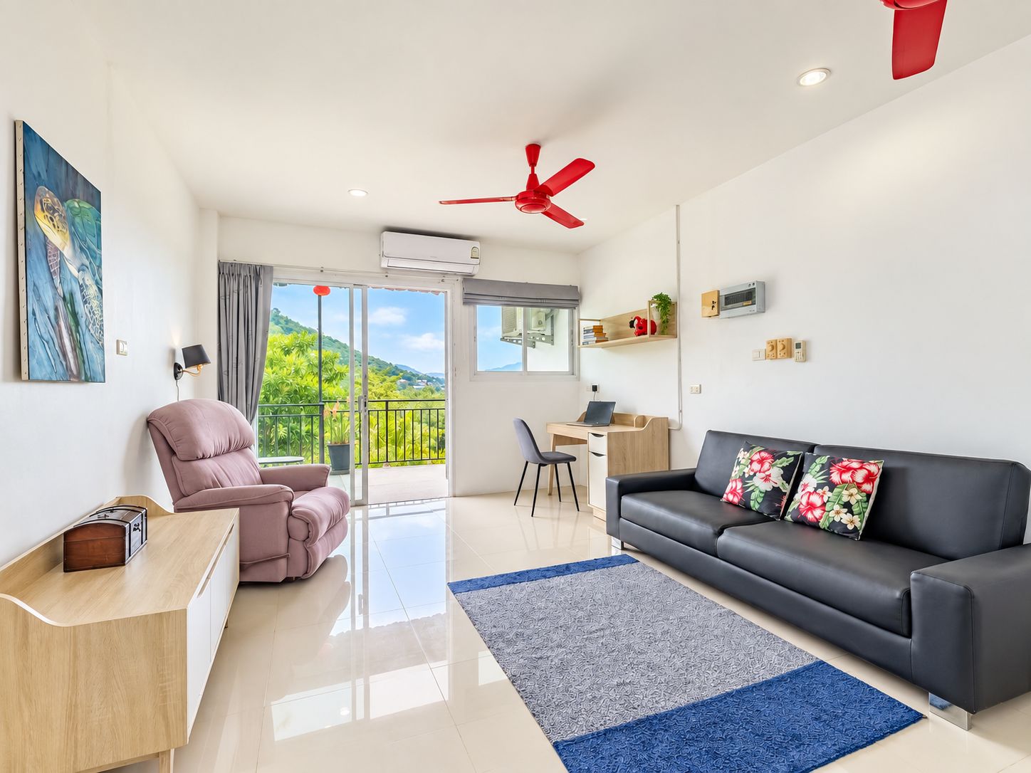Ein modernes Wohnzimmer mit einer Couch, einem Sessel, einem Schreibtisch und einem Balkon mit Blick auf Grünflächen.