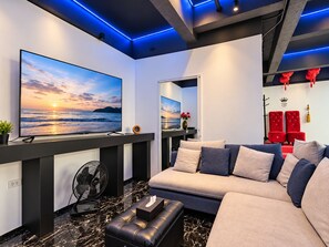 A modern living room with a large flat-screen TV, a sofa, and a fan. - Private Pool Villa for your family and friends (Tambon Chalong)