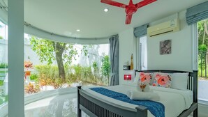 A modern bedroom with a curved ceiling, a bed with floral pillows, a red ceiling fan, and a view of greenery outside. - Private Pool Villa for your family and friends / Private Chef available (Tambon Chalong)
