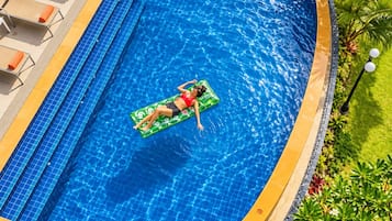 Ein Schwimmbecken mit einer Person auf einem Schwimmrowen, umgeben von Liegestühlen und Grünpflanzen.