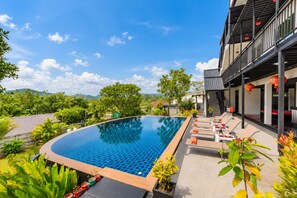 A swimming pool with lounge chairs and potted plants, surrounded by greenery and a building with balconies. - Private Pool Villa for your family and friends (Tambon Chalong)