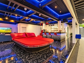 A modern hotel room with a red bed, a bar area, and a large TV screen. - Private Pool Villa for your family and friends (Tambon Chalong)