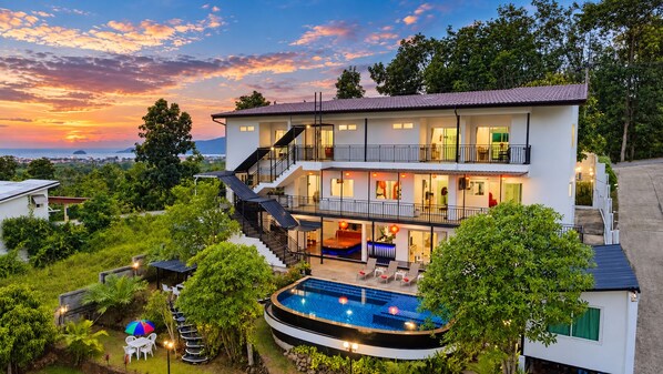 Une maison à deux étages avec une piscine, un espace salon extérieur et un balcon.