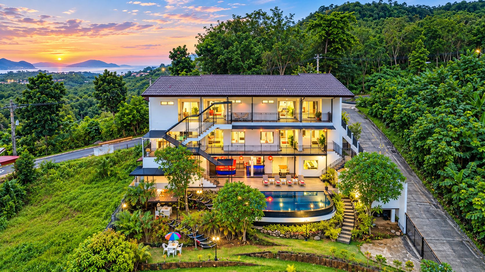 Ein mehrstöckiges Hotel mit Swimmingpool, umgeben von üppiger Vegetation und Blick auf den Sonnenuntergang.