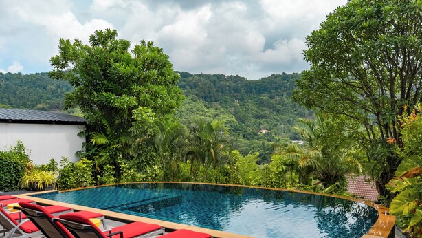 A rectangular swimming pool with red lounge chairs, surrounded by lush greenery and a mountainous backdrop. - Private Pool Villa for your family and friends / Private Chef available (Tambon Chalong)