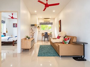 A modern living room with a sofa, a desk, and a chair. There is a red ceiling fan, a window with a view, and a bed in the adjacent room. - Private Pool Villa for your family and friends / Private Chef available (Tambon Chalong)