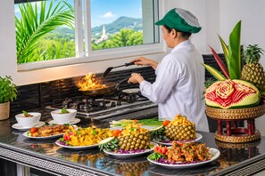 Une cuisine équipée d’une cuisinière, une personne en train de cuisiner et divers plats disposés sur le plan de travail.