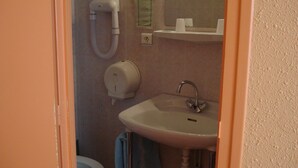 A bathroom with a toilet, a sink, a hand dryer, and a paper towel dispenser.