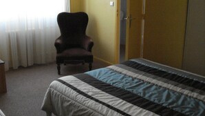 A bedroom with a bed, a chair, a wardrobe, and a window with curtains.