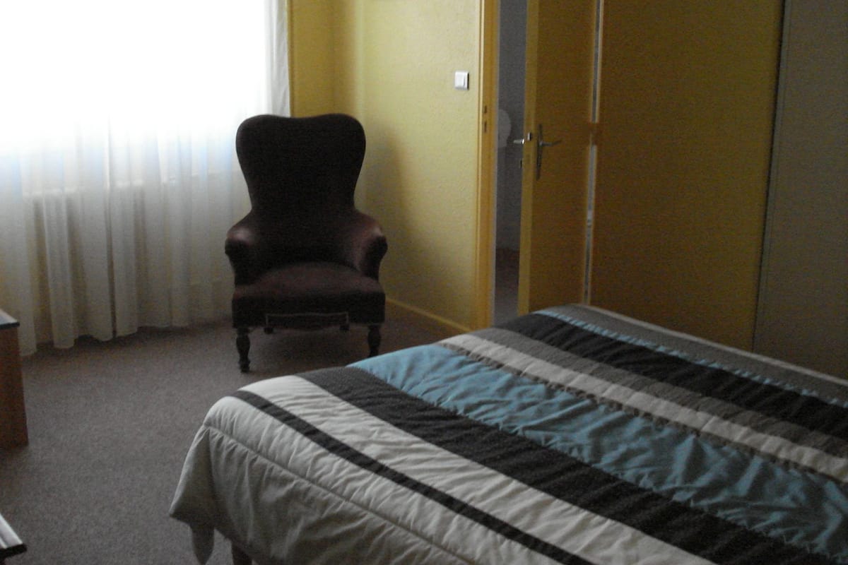Een slaapkamer met een bed, een stoel, een kledingkast en een raam met gordijnen.