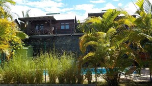 A wooden building with a balcony, surrounded by palm trees and a swimming pool. - Les Vanilliers (Saint-Joseph)