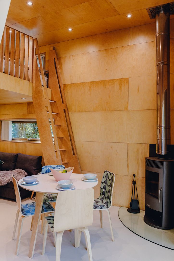 A modern interior with a wooden staircase, a dining area with a round table and chairs, and a wood-burning stove.