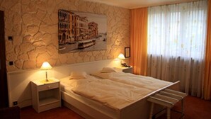 A bedroom with a stone wall, a bed with white bedding, two bedside tables with lamps, and a window with curtains. - Hotel Die Post in Bürgel GmbH (Offenbach am Main)