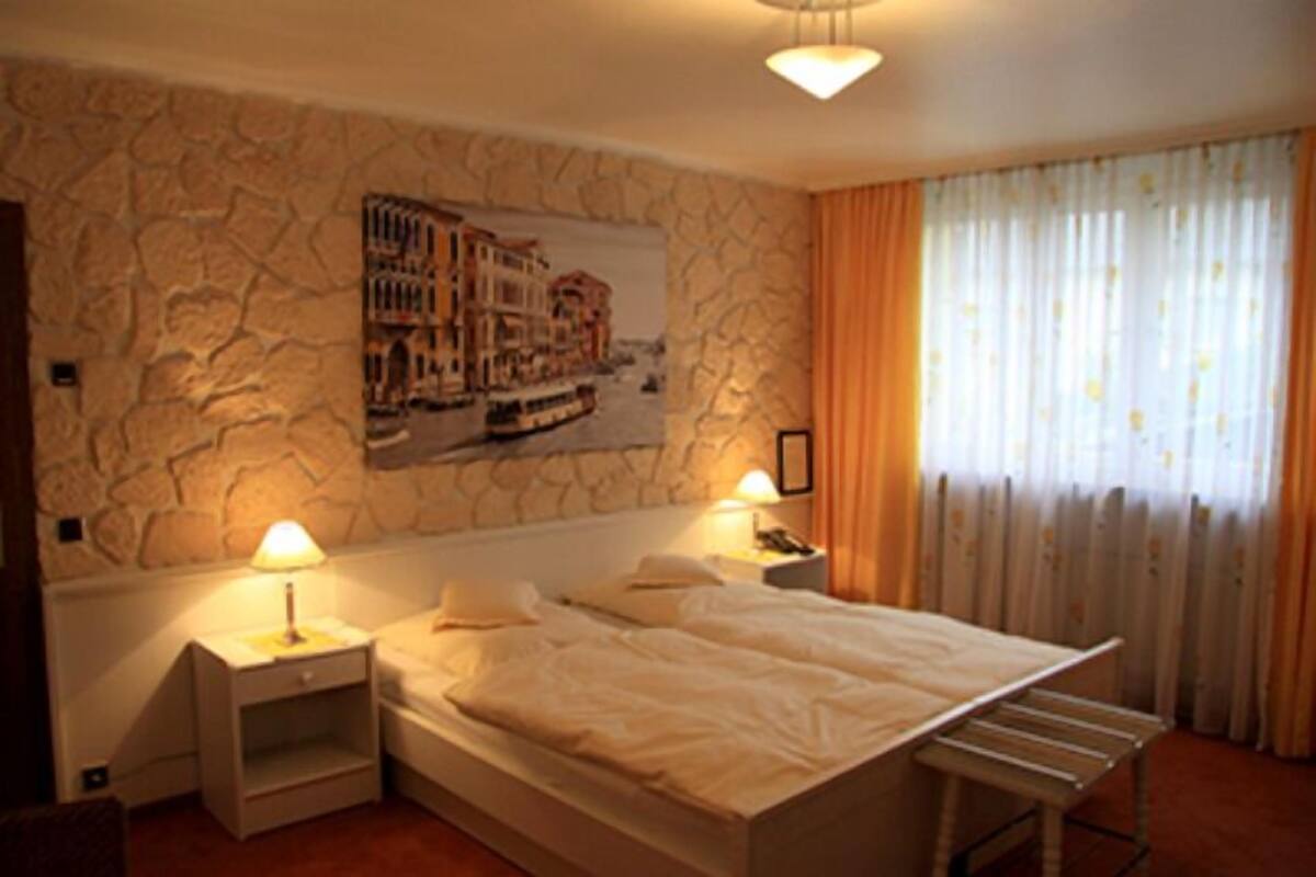 A bedroom with a stone wall, a bed with white bedding, two bedside tables with lamps, and a window with curtains.