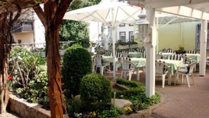 An outdoor patio area with tables and chairs, surrounded by stone walls and greenery. - Hotel Die Post in Bürgel GmbH (Offenbach am Main)