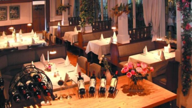 A restaurant with multiple tables, each set with white tablecloths and candles. There are bottles of wine on the tables, and a vase with flowers on one table. - Hotel Die Post in Bürgel GmbH (Offenbach am Main)