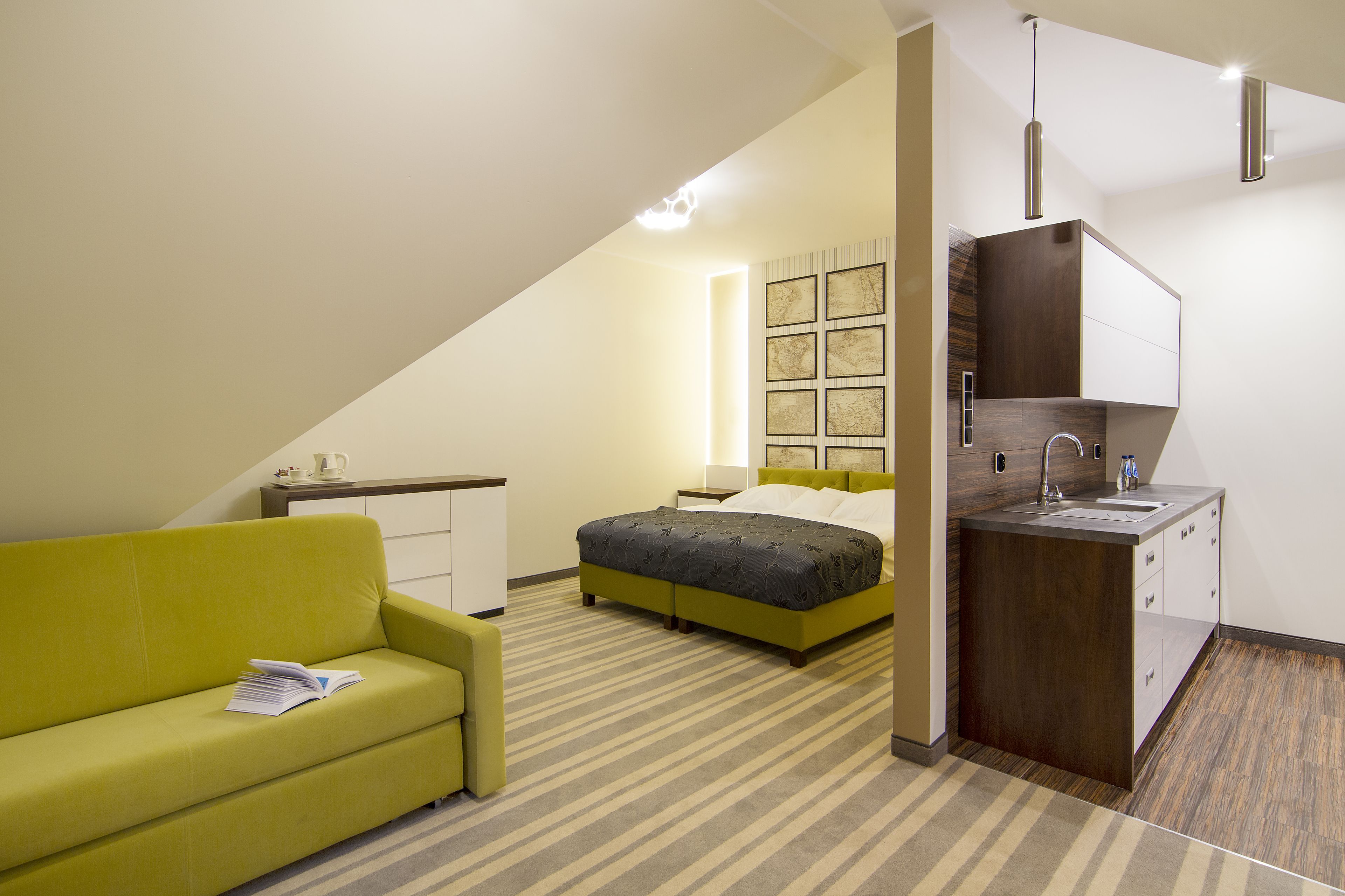 Una habitación de hotel compacta con una cama, una pequeña kitchenette, un sofá y una mesita de noche.