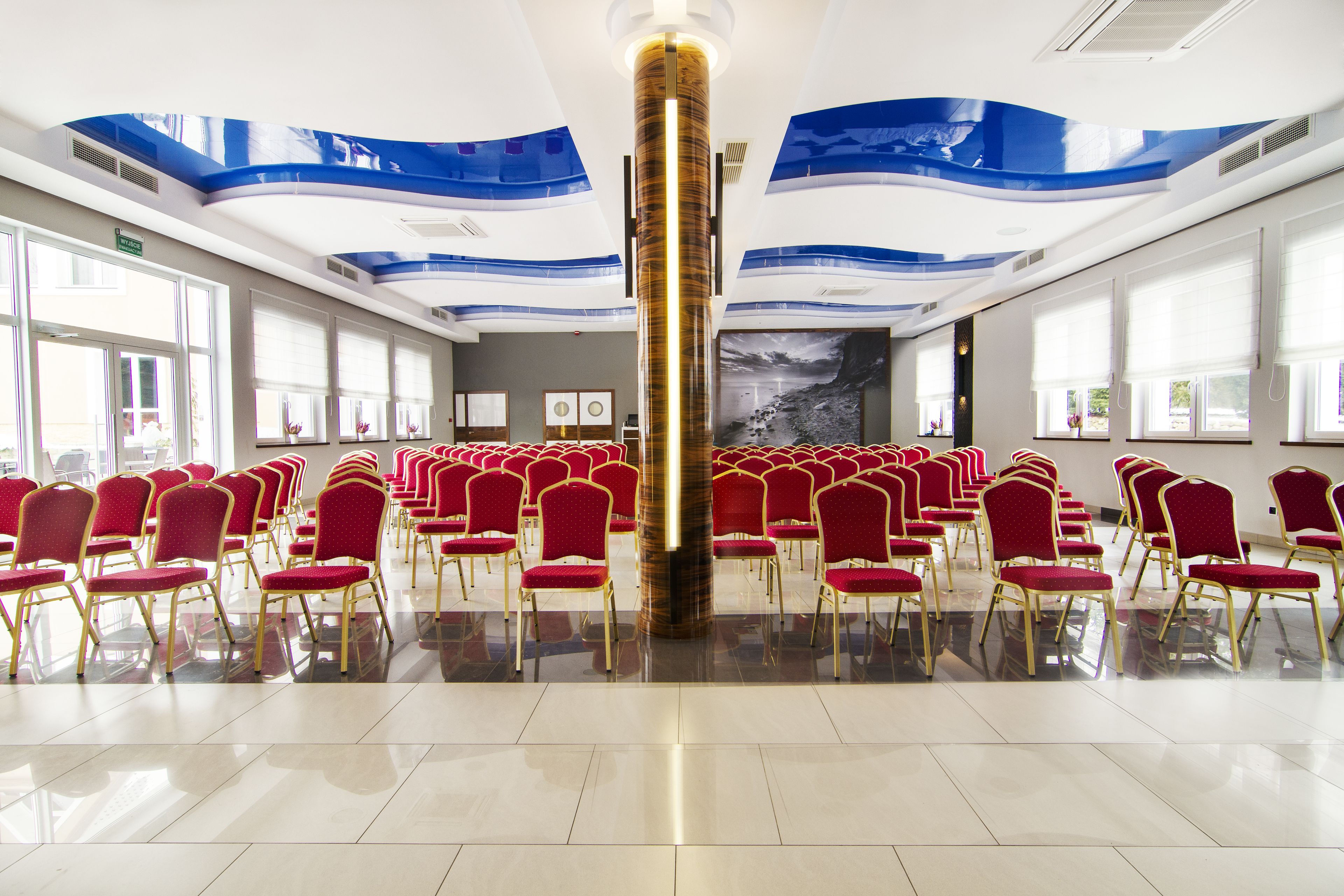 A spacious hall with rows of red chairs and a central pillar.