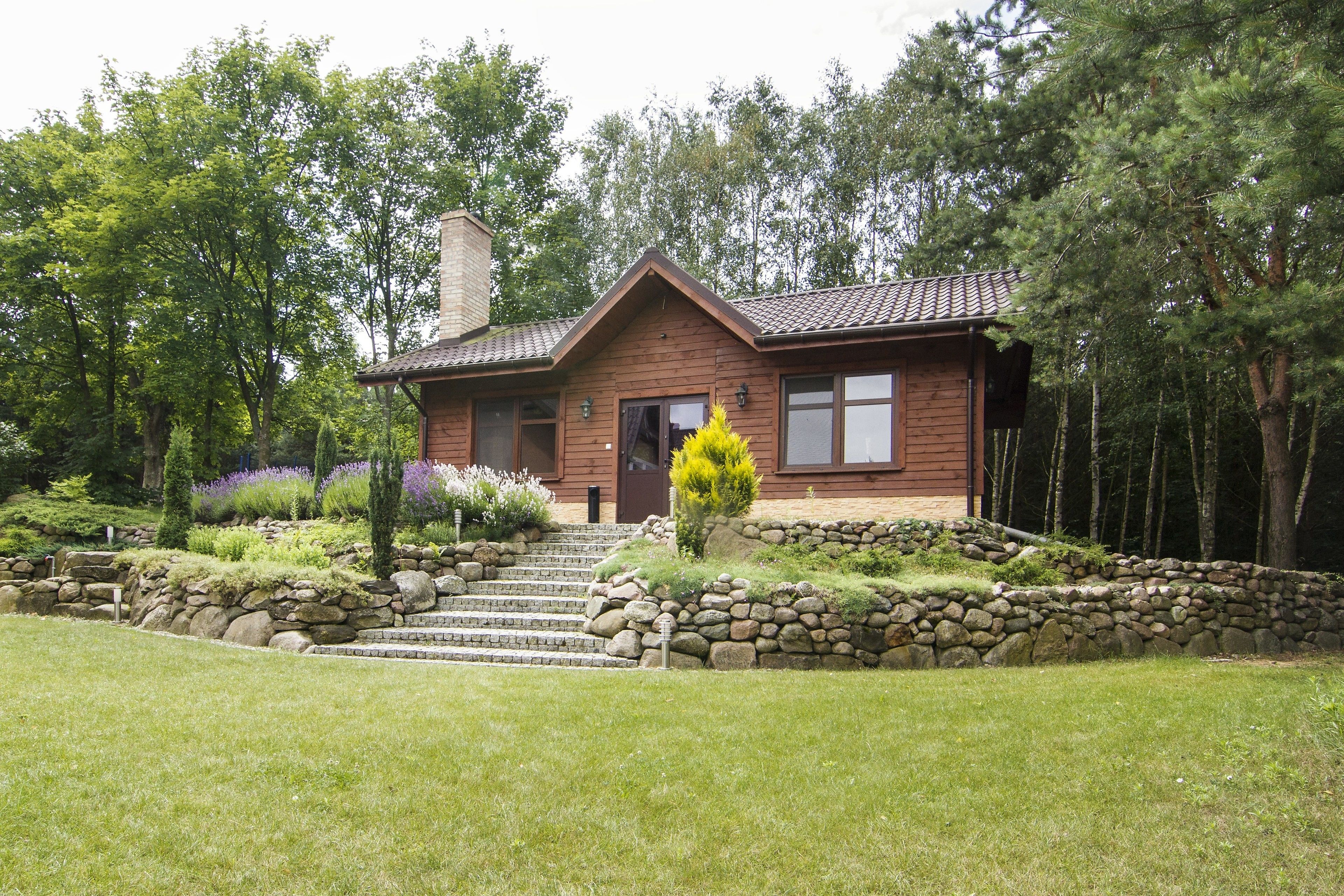 A wooden house with a stone staircase leading to the entrance, surrounded by greenery and trees.