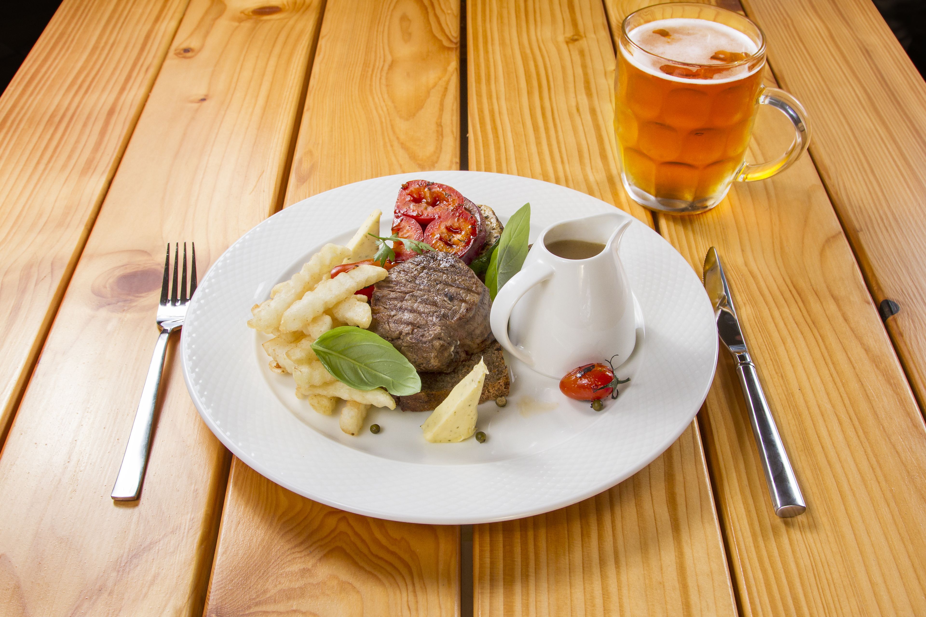 Un plato de comida con un filete, papas fritas y un tomate sobre una mesa de madera.